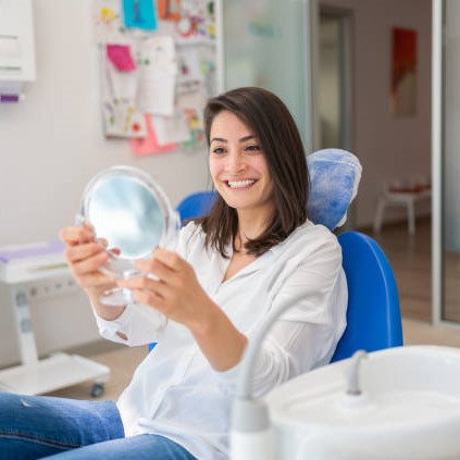 Young Woman Looking At Mirror With Smile In Dentist’s Office